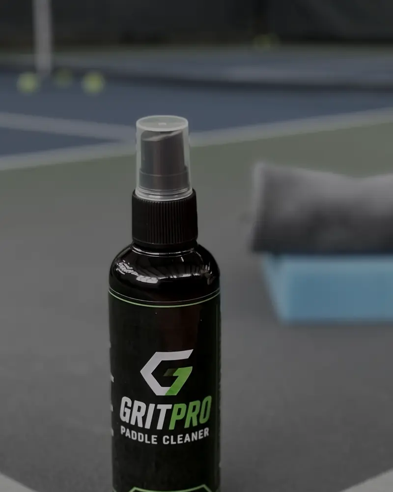 A GritPro Paddle Cleaner bottle standing on the line of a pickleball court